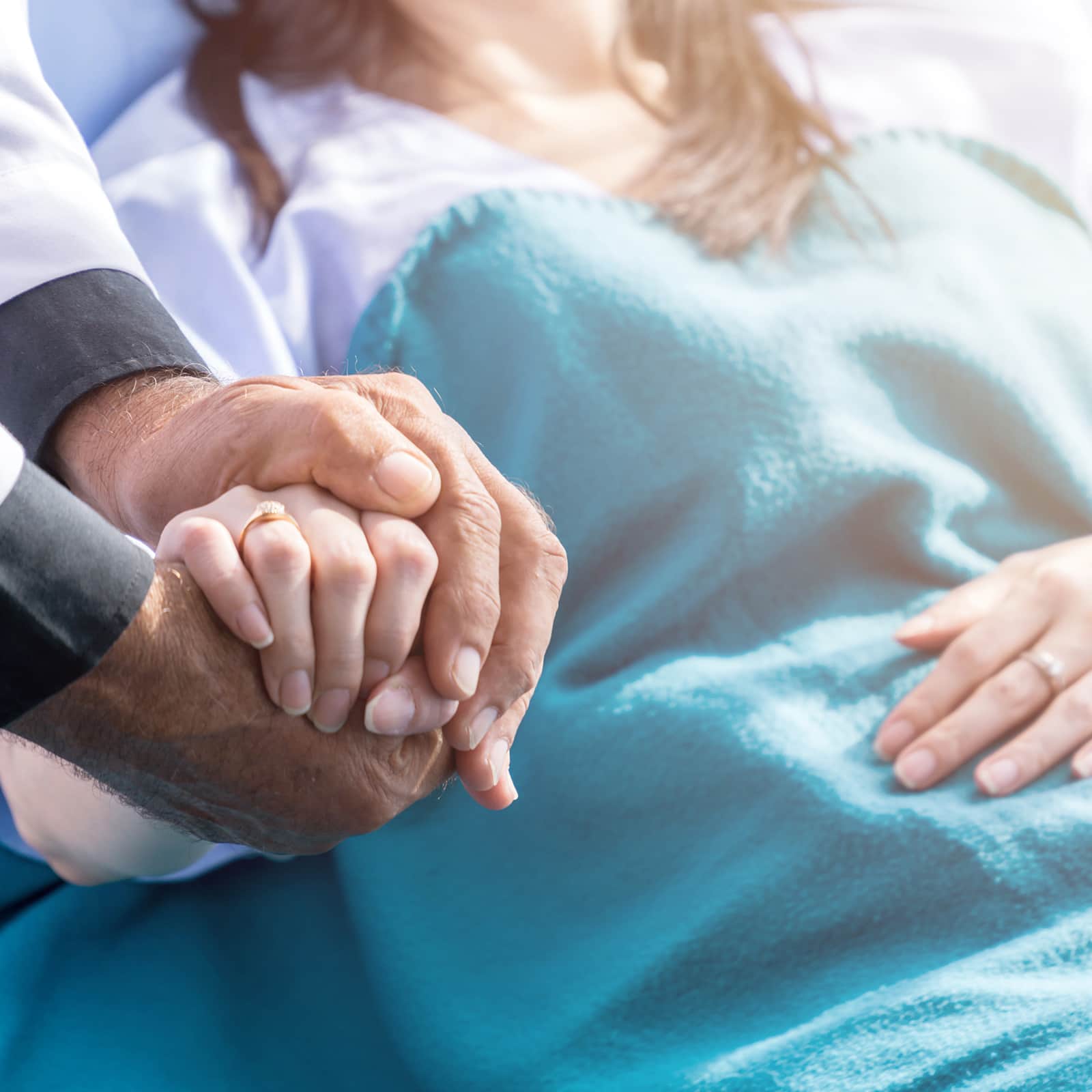 Male doctor holding female patient hand on the hospital bed.
