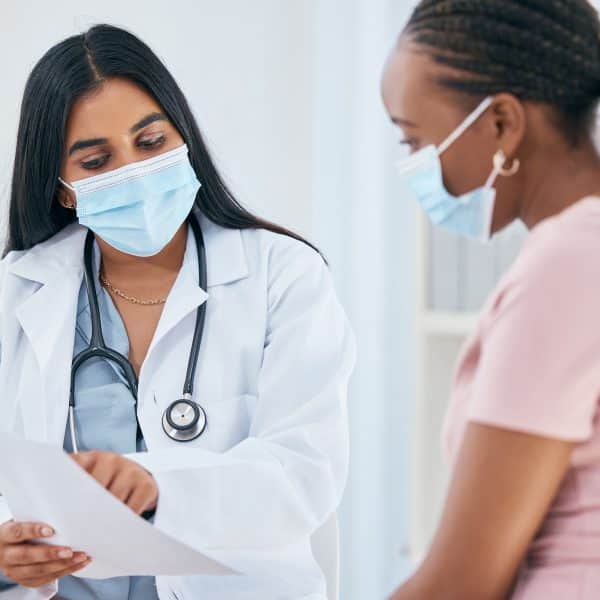 Doctor, covid mask and woman patient medical results in a health consultation in a clinic office. Diversity of women in a hospital, nurse and healthcare appointment with coronavirus consulting check