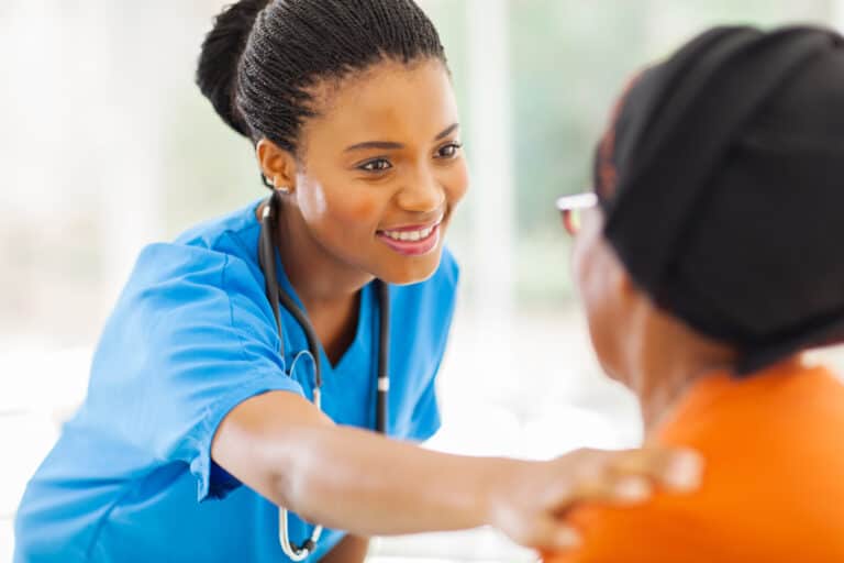 Nurse smiling and comforting a patient in a healthcare setting.