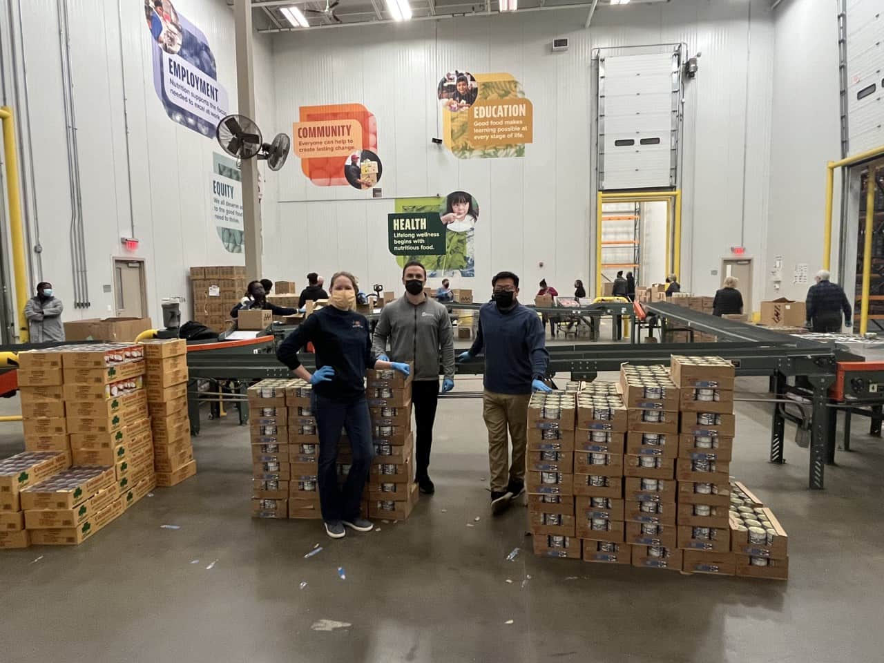A group of three people standing in a warehouse with stacks of boxes and conveyor belts.