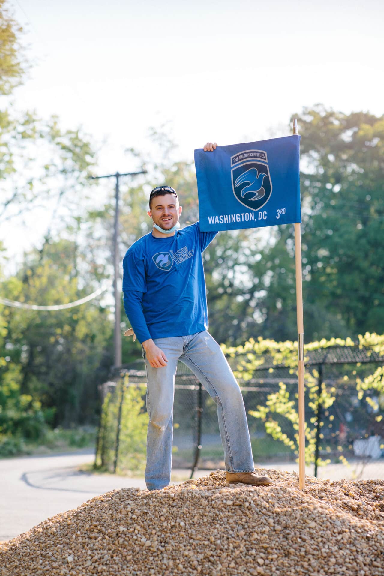 Man standing on a mound holding a Washington, DC flag outdoors.