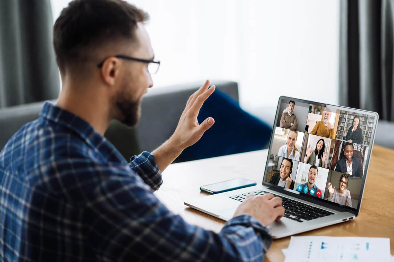 Man participating in a virtual meeting on a laptop with multiple colleagues.