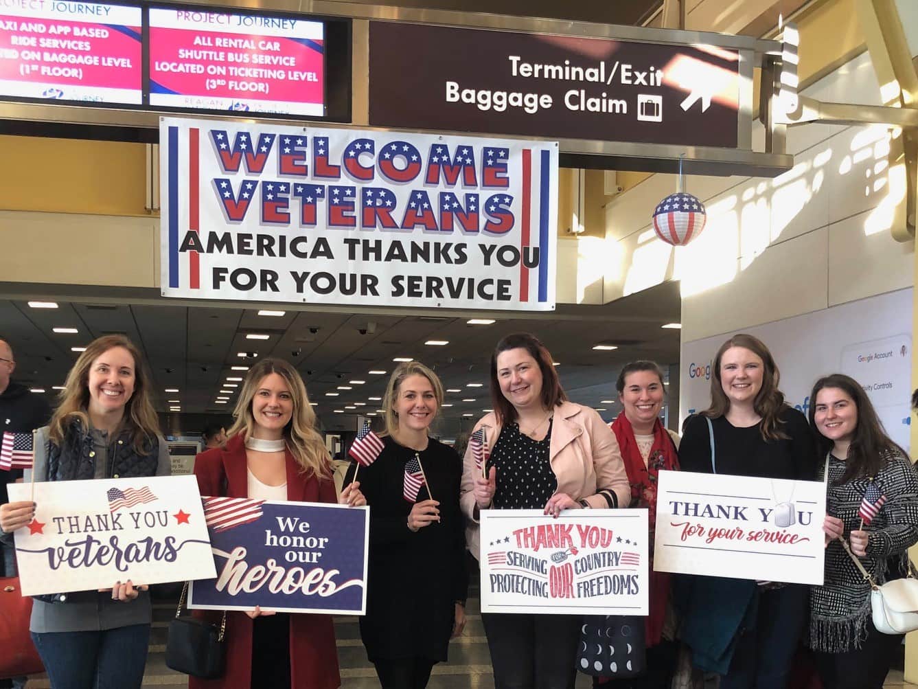 Group of women holding thank you signs for veterans at airport.