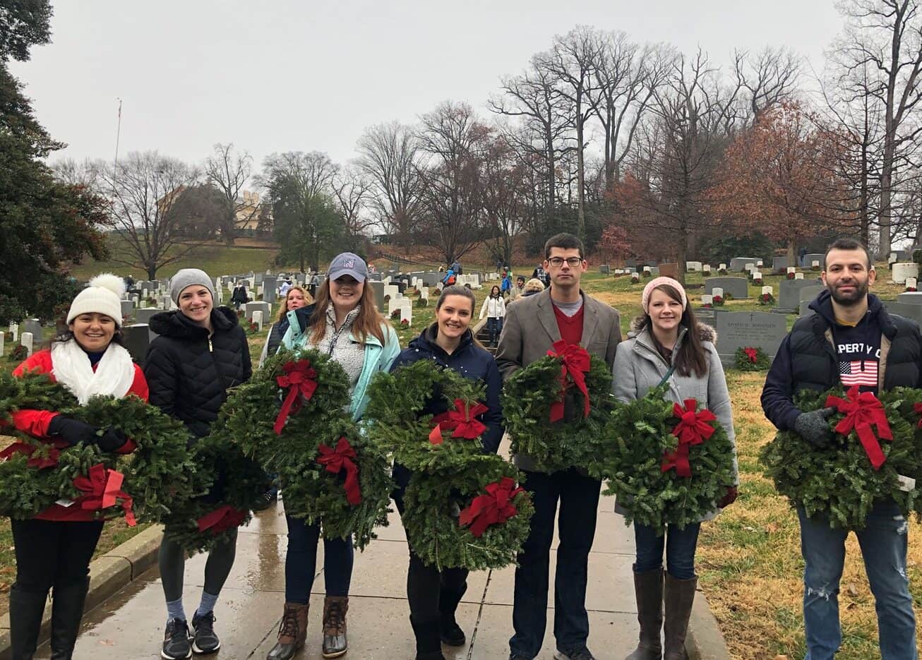 Group of people holding wreaths at a cemetery during a memorial event.
