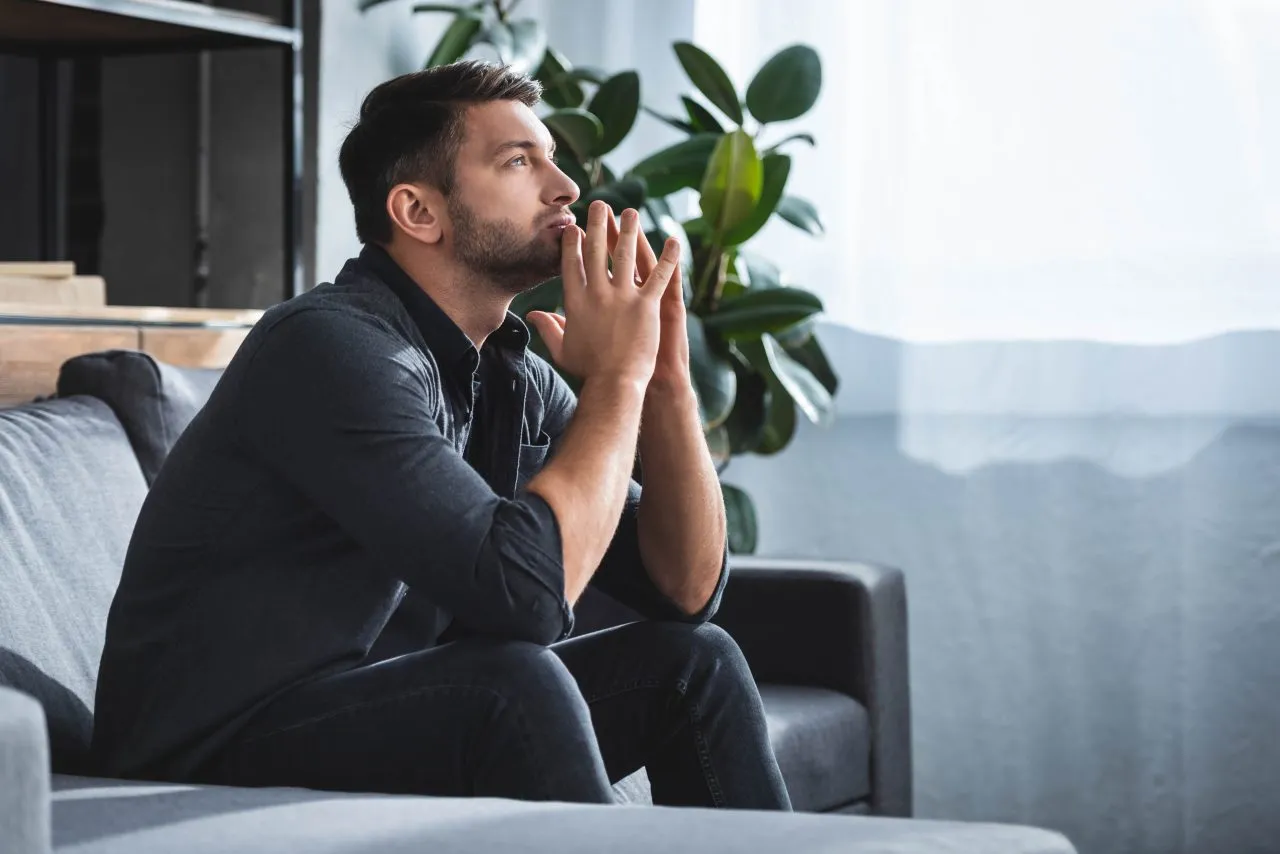 side view of handsome and pensive man sitting on sofa and lookin