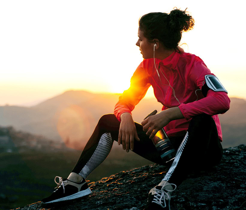 Young woman resting after outdoor run at sunset with camera and headphones.