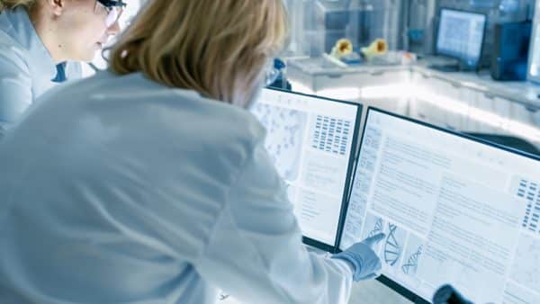 Scientists analyze data on multiple computer screens in a laboratory setting.