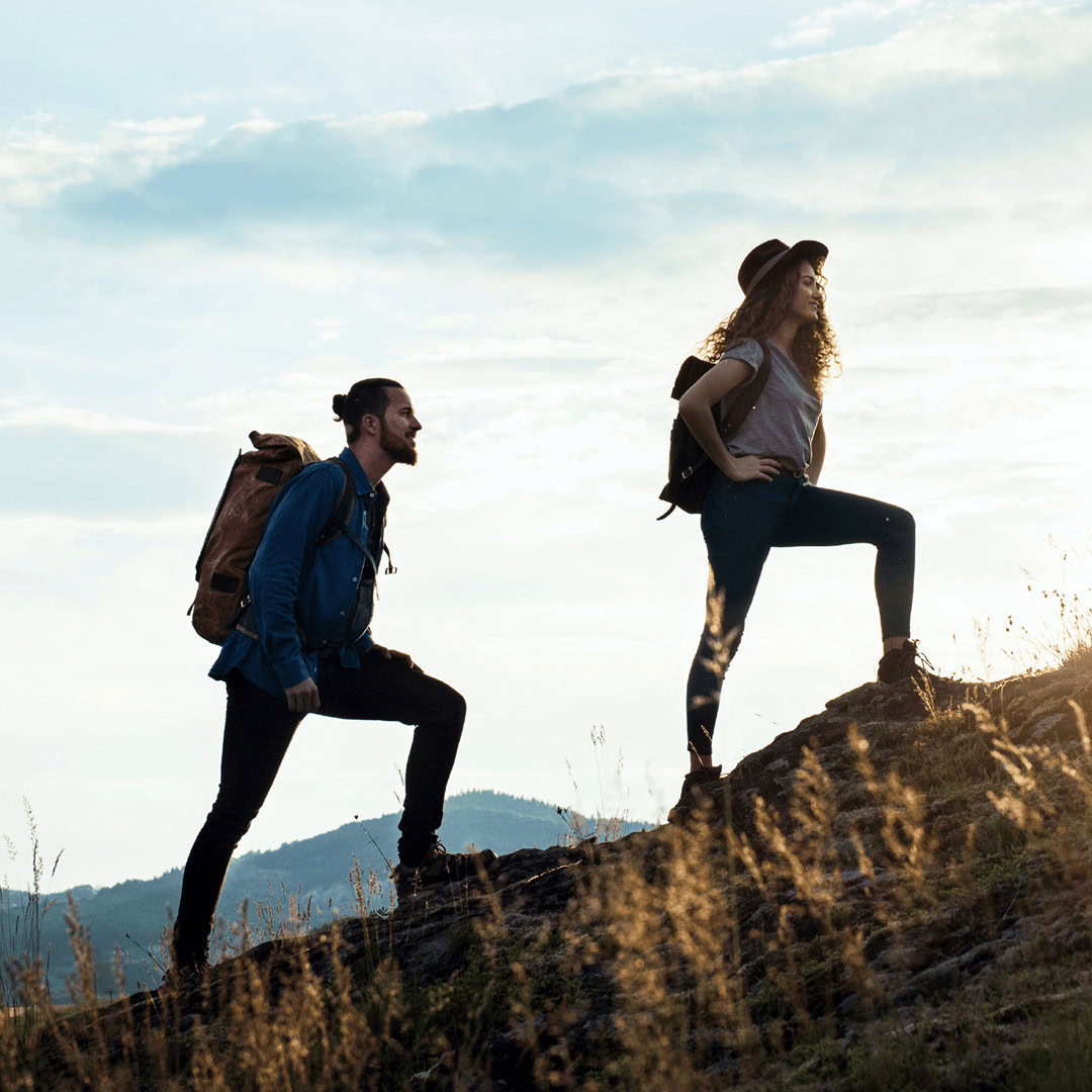 Two hikers with backpacks climbing a mountain trail at sunset.