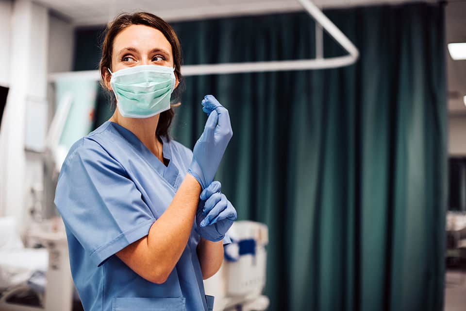 Healthcare professional in scrubs and mask preparing for patient care.