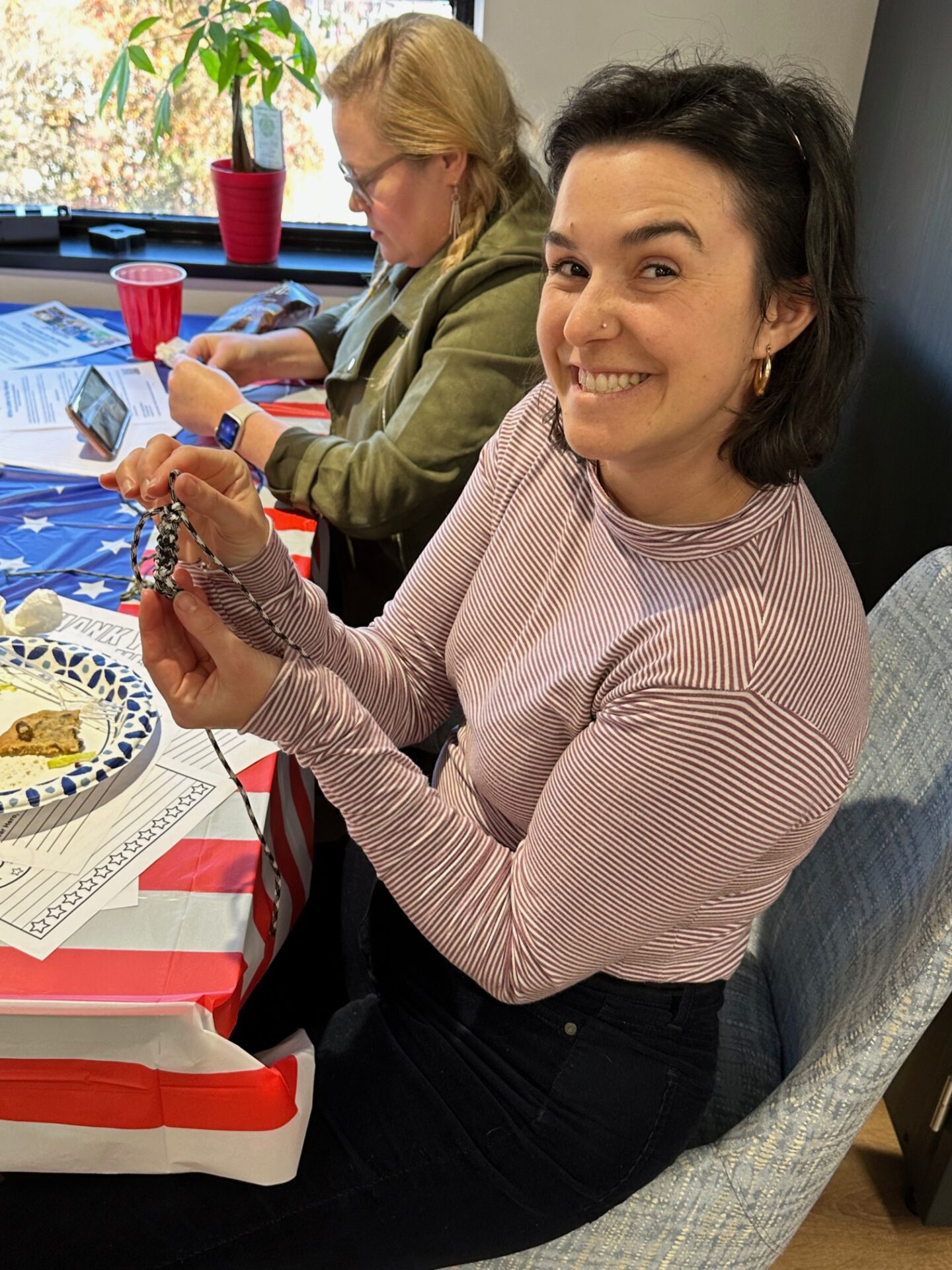 Two women at a table, one smiling and holding a small item, the other focused on her phone.