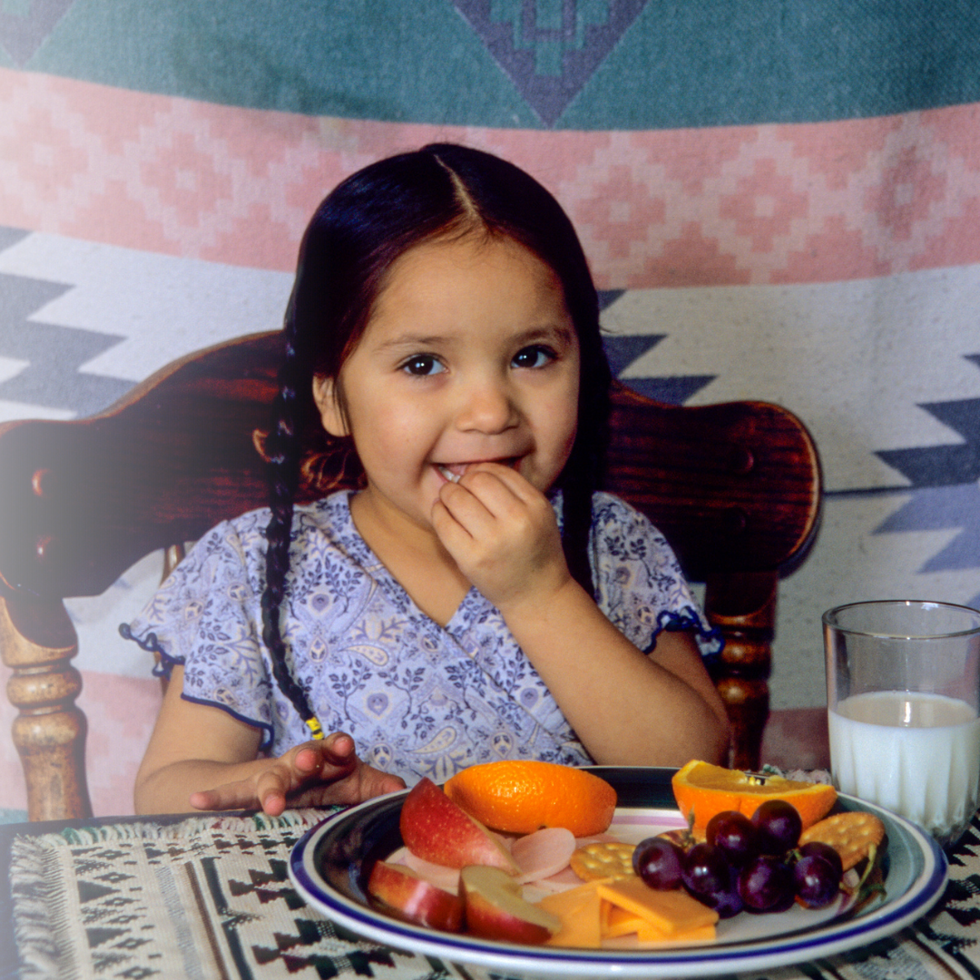 Young girl enjoying a healthy breakfast with fruit and milk at a table.