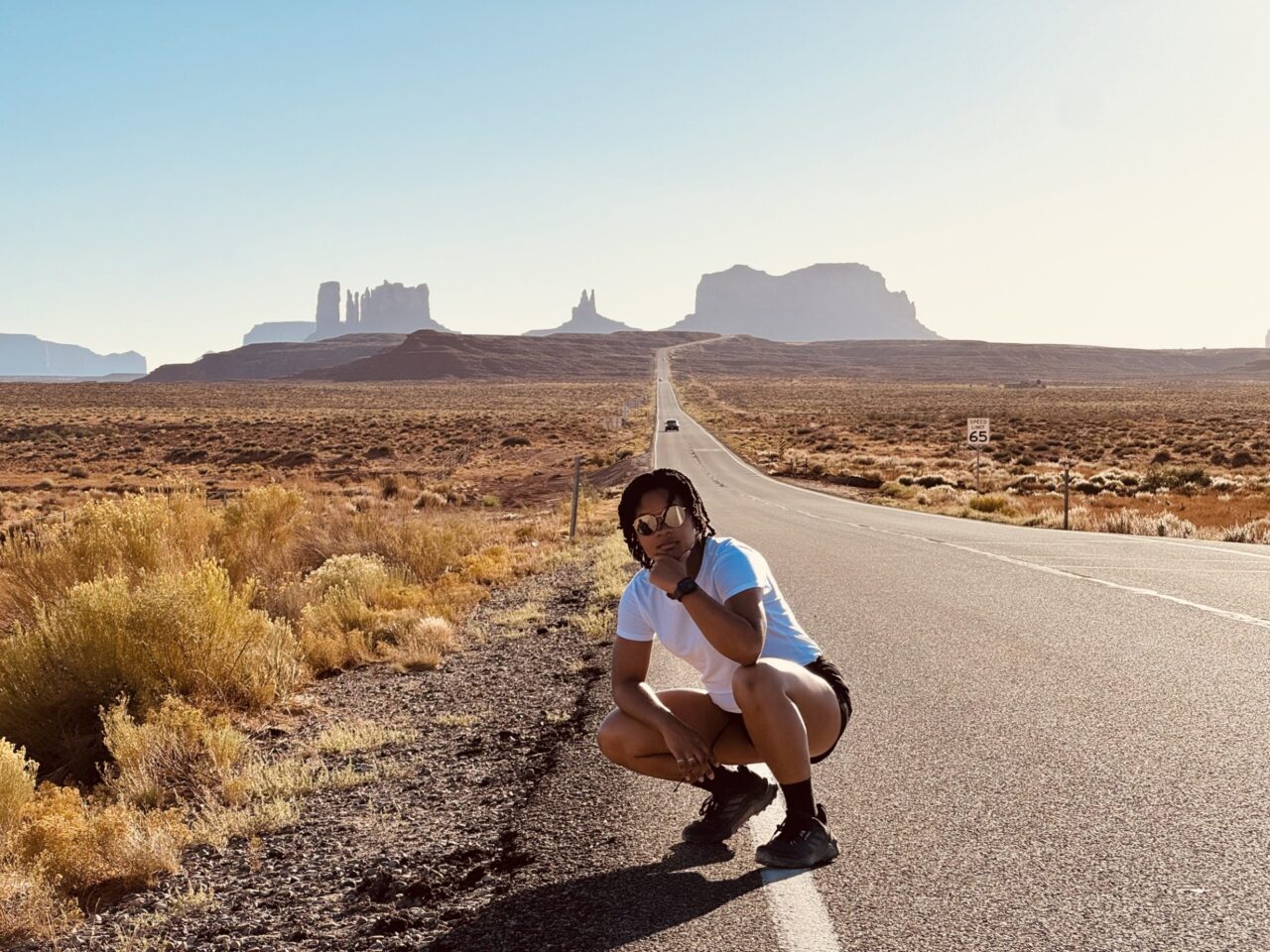 Woman crouching on the side of a desert highway with Monument Valley in the background.