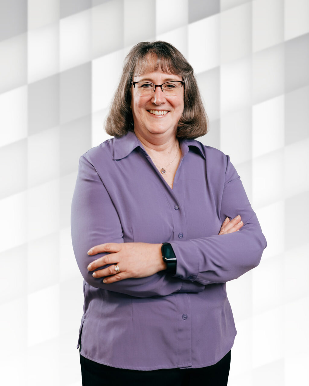 Professional woman smiling with arms crossed in front of modern window background.